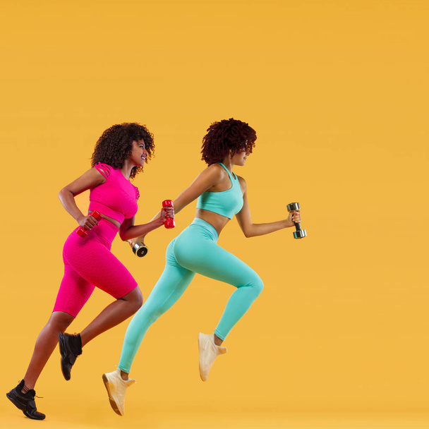 Strong athletic, woman sprinter or runner, running on yellow background with dumbbells wearing sportswear. Fitness and sport motivation. - 写真・画像