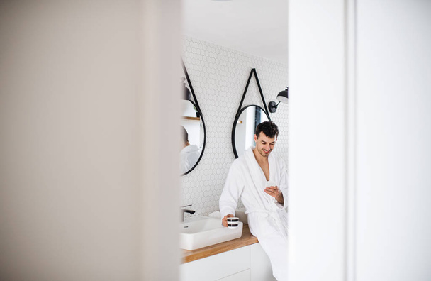 Young man with smartphone in the bathroom in the morning. - Φωτογραφία, εικόνα
