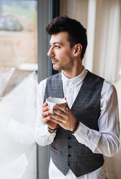 Young man with coffee standing by the window. Copy space. - Zdjęcie, obraz