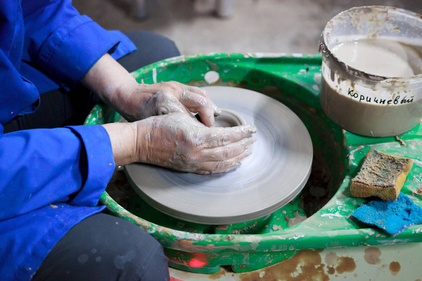 Student začátečník v první lekci keramiky se snaží vyrobit výrobek z hlíny na hrnčířském kole. reportáž. Nesprávné nastavení ruky - Fotografie, Obrázek