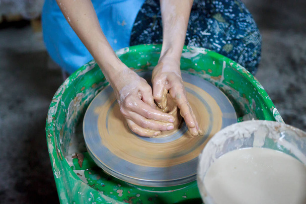 A novice student in the first lesson in pottery tries to make a product from clay on a potter's wheel. reportage. Incorrect hand setting - Photo, image