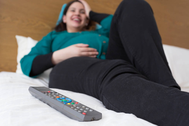 Aanstaande moeder ontspannen kijken naar televisie en lachen - Foto, afbeelding