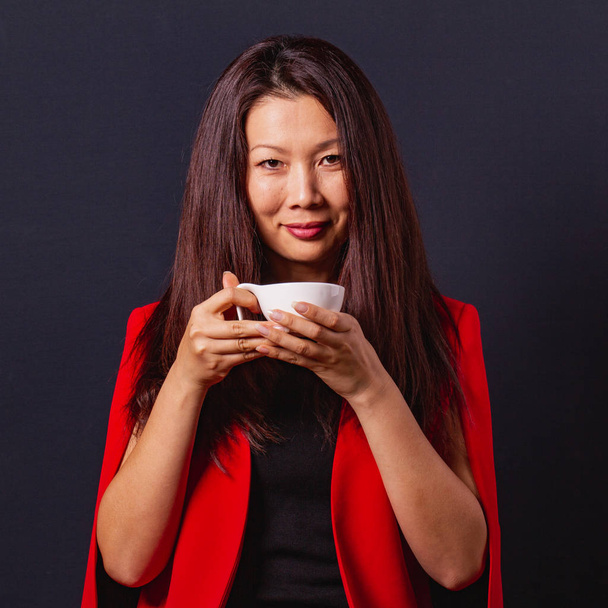 Элегантная милая азиатская женщина с длинными волосами держит чашку кофе в час
 - Фото, изображение