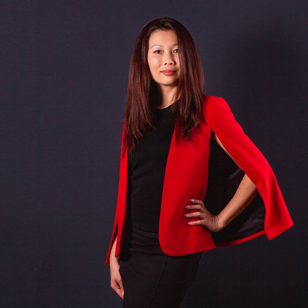 Beautiful Asian brunette in red jacket standing on a dark backgr - Photo, Image