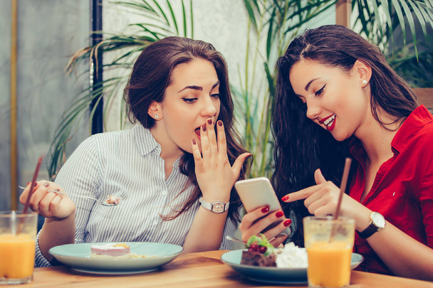  Two young women eating cakes and using phone in cafe - Foto, Bild