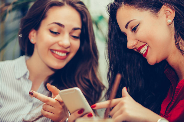 Deux jeunes femmes partageant les médias sociaux dans un téléphone intelligent au café
 - Photo, image