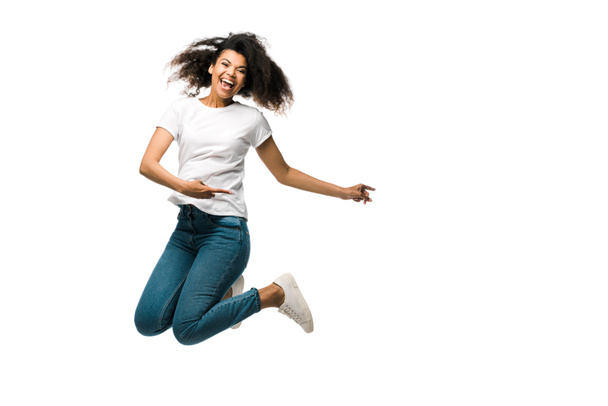 mujer afro-americana positiva señalando con los dedos y saltando aislada sobre blanco
  - Foto, Imagen