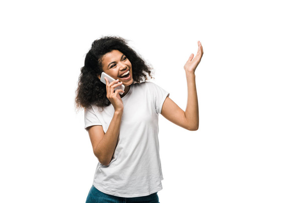 cheerful and curly african american girl talking on smartphone and gesturing isolated on white  - Fotoğraf, Görsel