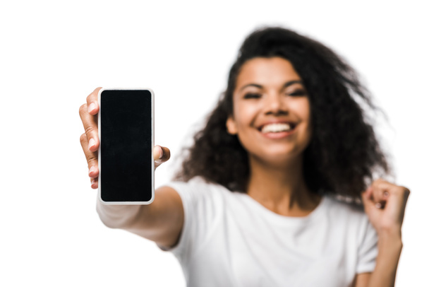 selectieve focus van positieve Afro-Amerikaanse meisje houden smartphone met blanco scherm en vieren geïsoleerd op wit  - Foto, afbeelding
