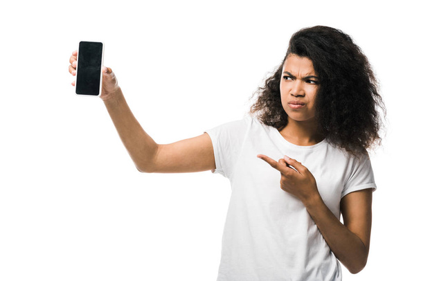 displeased african american girl pointing with finger at smartphone with blank screen isolated on white  - Foto, Imagem