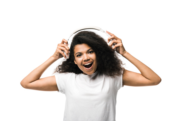 positive african american girl holding headphones while looking at camera isolated on white  - Zdjęcie, obraz