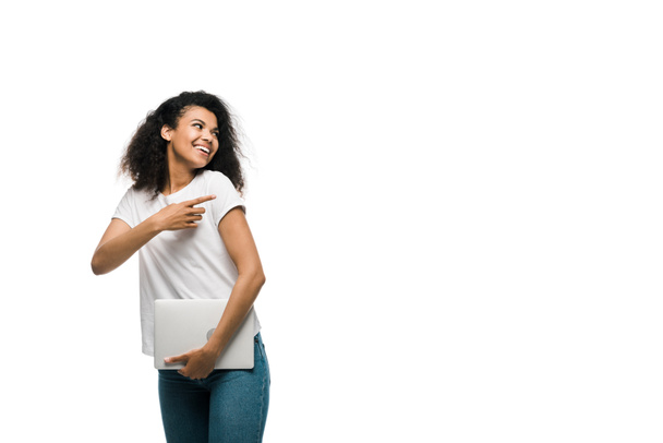 happy young african american woman pointing with finger while holding laptop isolated on white  - Foto, Imagen