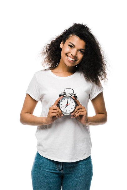cheerful curly african american girl holding vintage alarm clock isolated on white  - 写真・画像