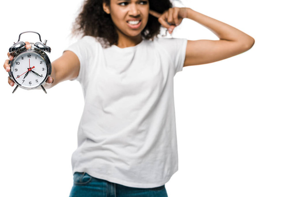 白で隔離された耳を覆う不愉快な巻き毛のアフリカ系アメリカ人の女の子の手にヴィンテージ目覚まし時計の選択的な焦点  - 写真・画像