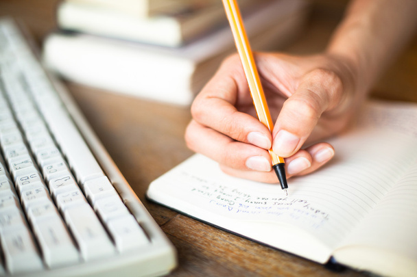 Mujer manos escribe un bolígrafo en un cuaderno, teclado de la computadora en el fondo
. - Foto, imagen