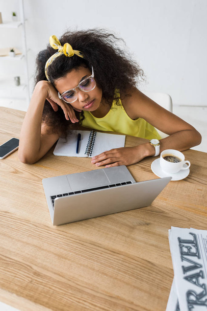 вид сверху на молодую африканскую американку в очках, смотрящую на ноутбук возле чашки кофе
  - Фото, изображение