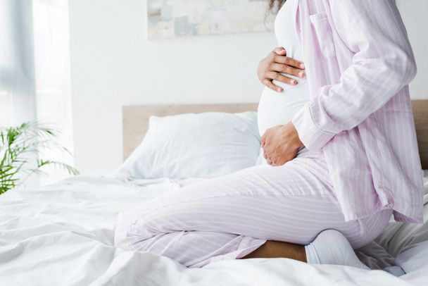 vue recadrée de la femme afro-américaine enceinte assise sur le lit et touchant le ventre
  - Photo, image