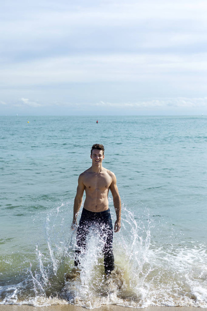 Young handsome muscular man on seashore in a sunny day - Φωτογραφία, εικόνα