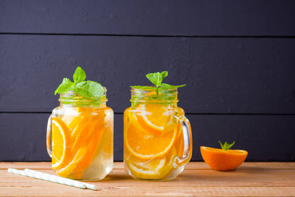 Infused water with orange, lemon and mint. Mug delicious refreshing drink of mix fruits with mint on wooden boards. Iced summer drink in mason jar. Homemade detox cocktail - Fotoğraf, Görsel