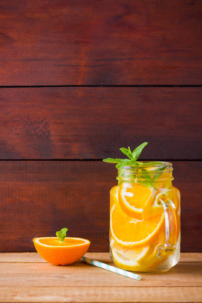 Fruit infused water with orange, lemon and mint. Mug delicious refreshing drink of mix fruits with mint on wooden boards. Iced summer drink in mason jar. Fresh homemade lemonade - Foto, Bild