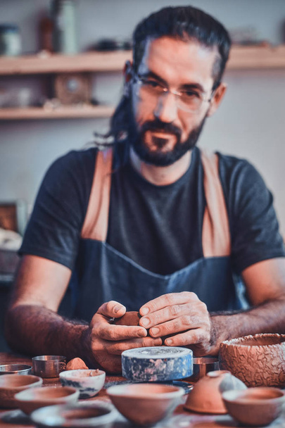 Diligent pensive man in glasses at his  pottery workshop is workig for new project. - Photo, Image