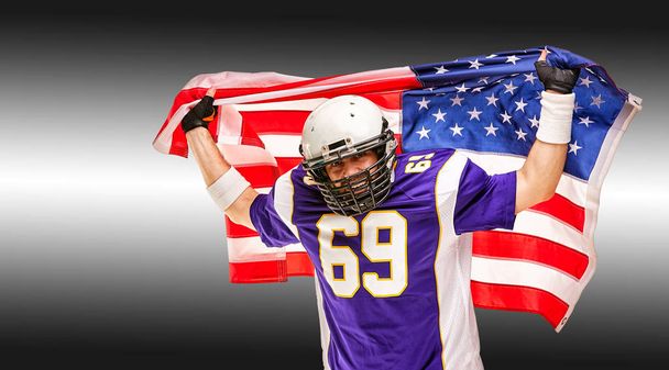 Retrato de primer plano de jugador de fútbol americano. Jugador de fútbol americano con una bandera americana en sus manos. Concepto patriotismo, celebración
. - Foto, imagen