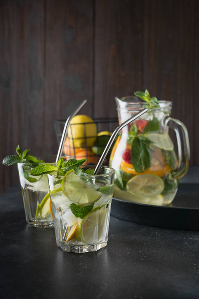 ライム、オレンジ、レモン、イチゴのガラスと瓶のデトックスレモネード。夏の健康的な新鮮な飲み物。暗い木製の背景. - 写真・画像