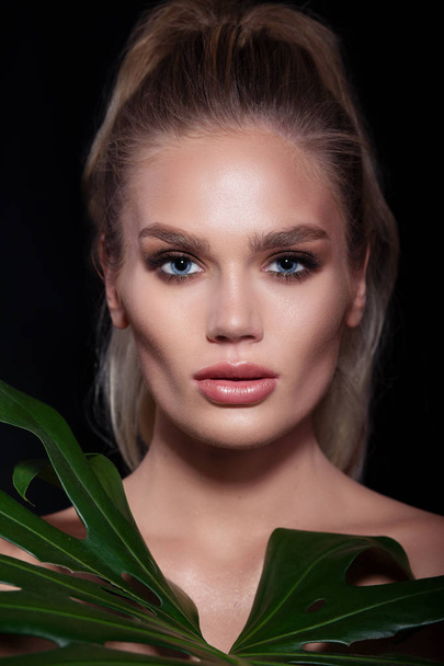 Beautiful woman face with fresh professional makeup in green leaves. - Фото, изображение