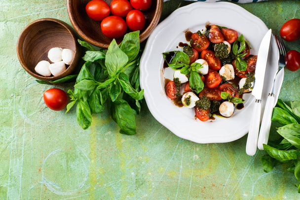 Свіжий італійський салат з помідорами, сиром мозарелла і песо подається на білій тарілці на зеленому обшарпаному столі. - Фото, зображення