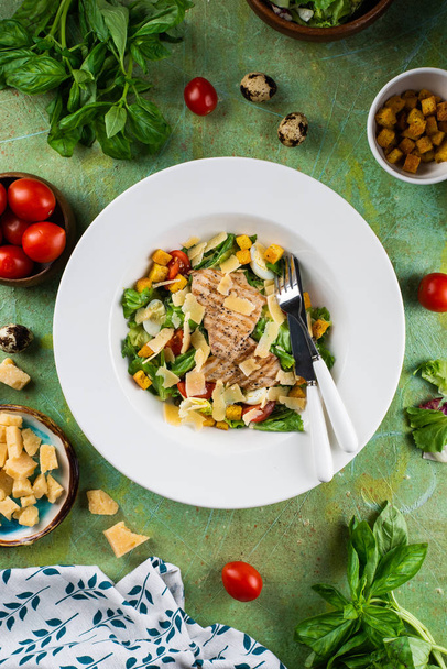 グリルチキン胸肉とパルメザンチーズの新鮮なスナックサラダは、食材と緑のみすぼらしいテーブルの白いプレートに提供 - 写真・画像