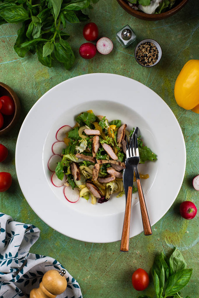 Verse snack salade met kip geserveerd op witte plaat op groene shabby tafel - Foto, afbeelding