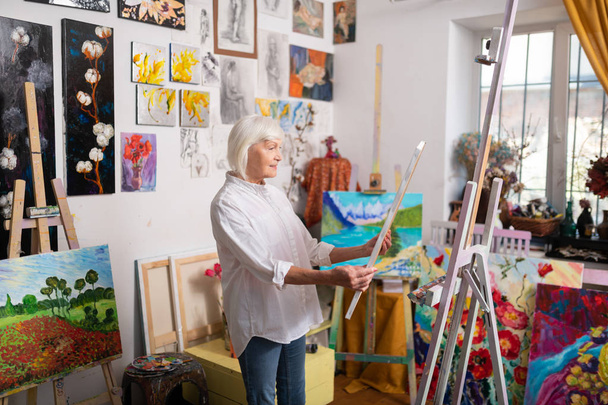 Talented mature artist feeling inspired looking at her picture - Фото, зображення