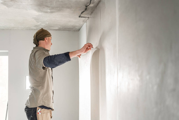 Pracovník použije list tapety. Muž lepí tapety na betonovou zeď. Opravte byt. Koncept renovace domu. Bílá tapeta na barvu. krok za krokem - Fotografie, Obrázek