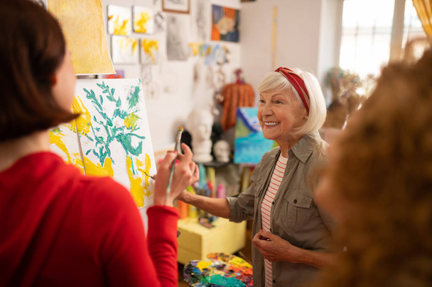 Χαρούμενη συνταξιούχος γυναίκα διδάσκει τους μαθητές της να ζωγραφίσει - Φωτογραφία, εικόνα