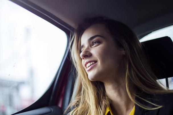 Bonita jovem empresária sentada no banco de trás de um carro e olhando para fora da janela
 - Foto, Imagem