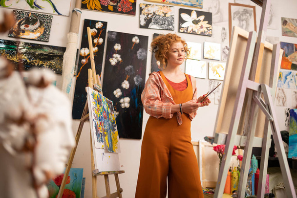 Artist wearing orange clothing standing near canvas - 写真・画像