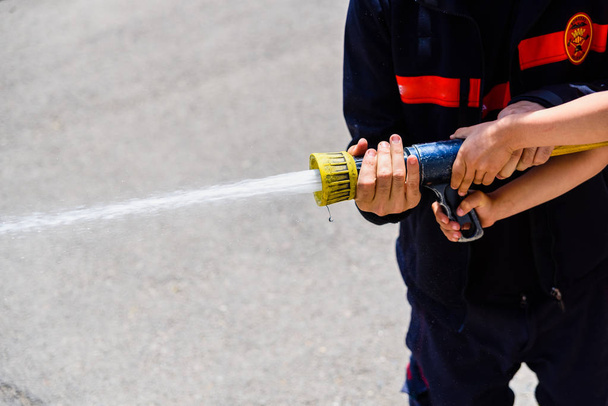 Firefighter demonstrating how to use a water hose to children du - Fotoğraf, Görsel