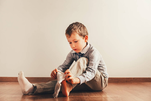 Το παιδί κάθεται στο πάτωμα βάζοντας τις κάλτσες του με ένα - Φωτογραφία, εικόνα