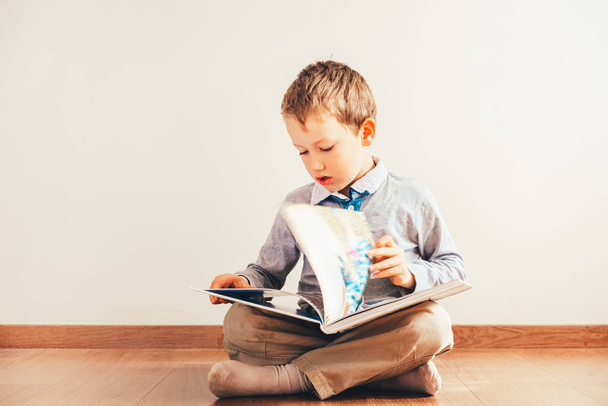 Boy sitting on the floor with reading a book on his knees, isola - Photo, Image