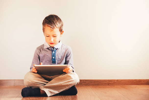 Boy sitting on the floor using a tablet absorbed in it. - Foto, immagini