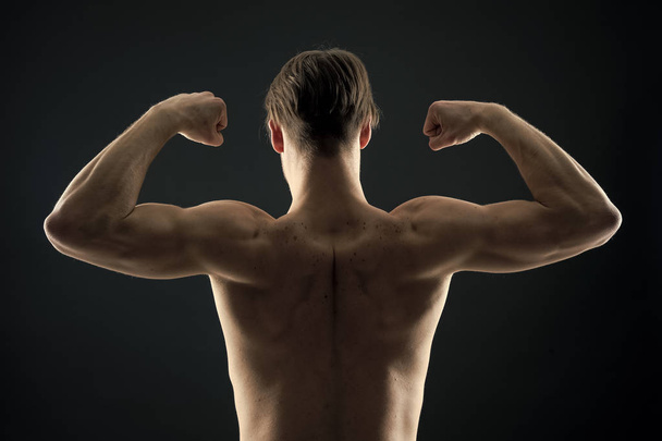 Athlete with fit torso, back view. Man bodybuilder flex arm muscles. Sportsman show biceps and triceps. Workout and training activity in gym. Power and strength concept - Photo, Image