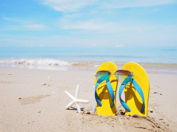 Sandalia amarilla sobre arena beige fondo playa verano
. - Foto, imagen