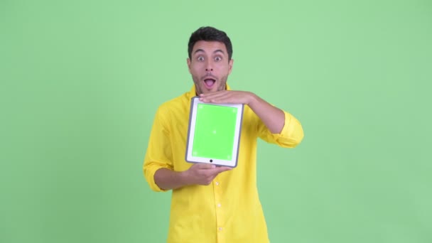 Happy young Hispanic businessman showing digital tablet and looking surprised - Imágenes, Vídeo