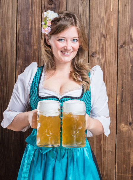 attractive young woman in traditional bavarian costume holding beer glasses and smiling at camera  - Zdjęcie, obraz