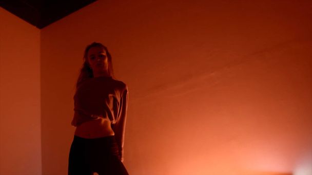 Νεαρή ελκυστική γυναίκα χορεύει στο σκοτεινό δωμάτιο. Πάμε. Επαγγελματίας χορευτής έντονα και παθιασμένα χορεύοντας σε μοντέρνο στυλ στο αμυδρά φωτισμένο δωμάτιο - Φωτογραφία, εικόνα