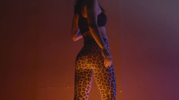 Rear view of beautiful model posing in sports leggings. Action. Beautiful model in sports leggings illuminated by neon light - Photo, Image