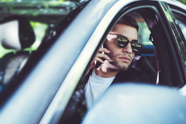 Mladý atraktivní muž pomocí mobilního telefonu v autě  - Fotografie, Obrázek