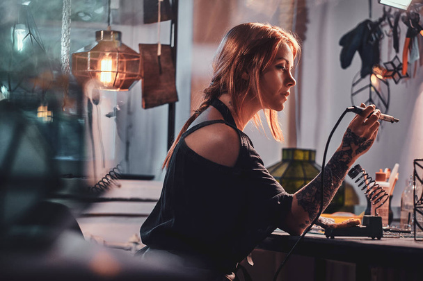 Attractive woman is doing soldering at her own artisan lamp studio. - Foto, Imagen