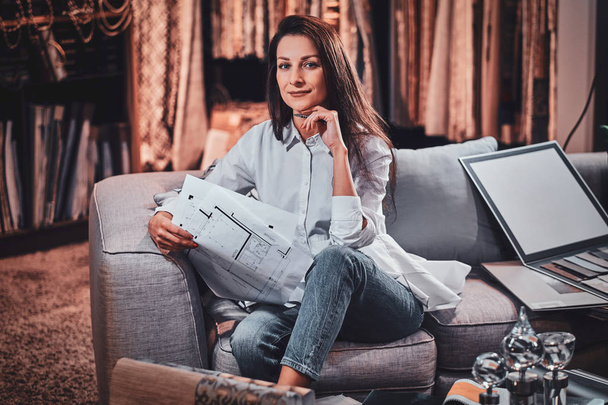 fröhliche Designerin sitzt auf dem Sofa in ihrem eigenen Kleidungsstudio - Foto, Bild