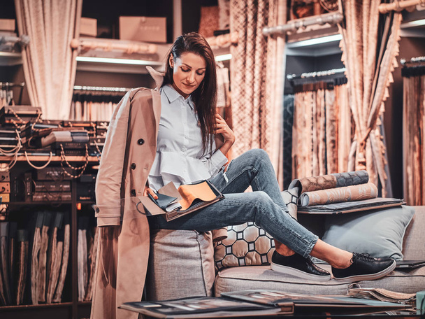 Diseñadora talentosa de moda está sentada en el sofá en su propio taller textil
 - Foto, Imagen